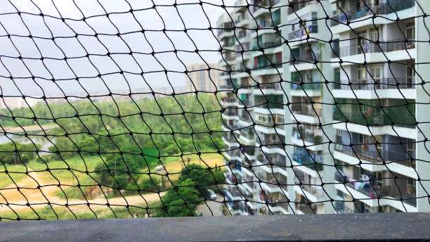 Stock photo of urban sprawl viewed through anti-bird netting on apartment balcony in Ghaziabad, India with cityscape view in background.